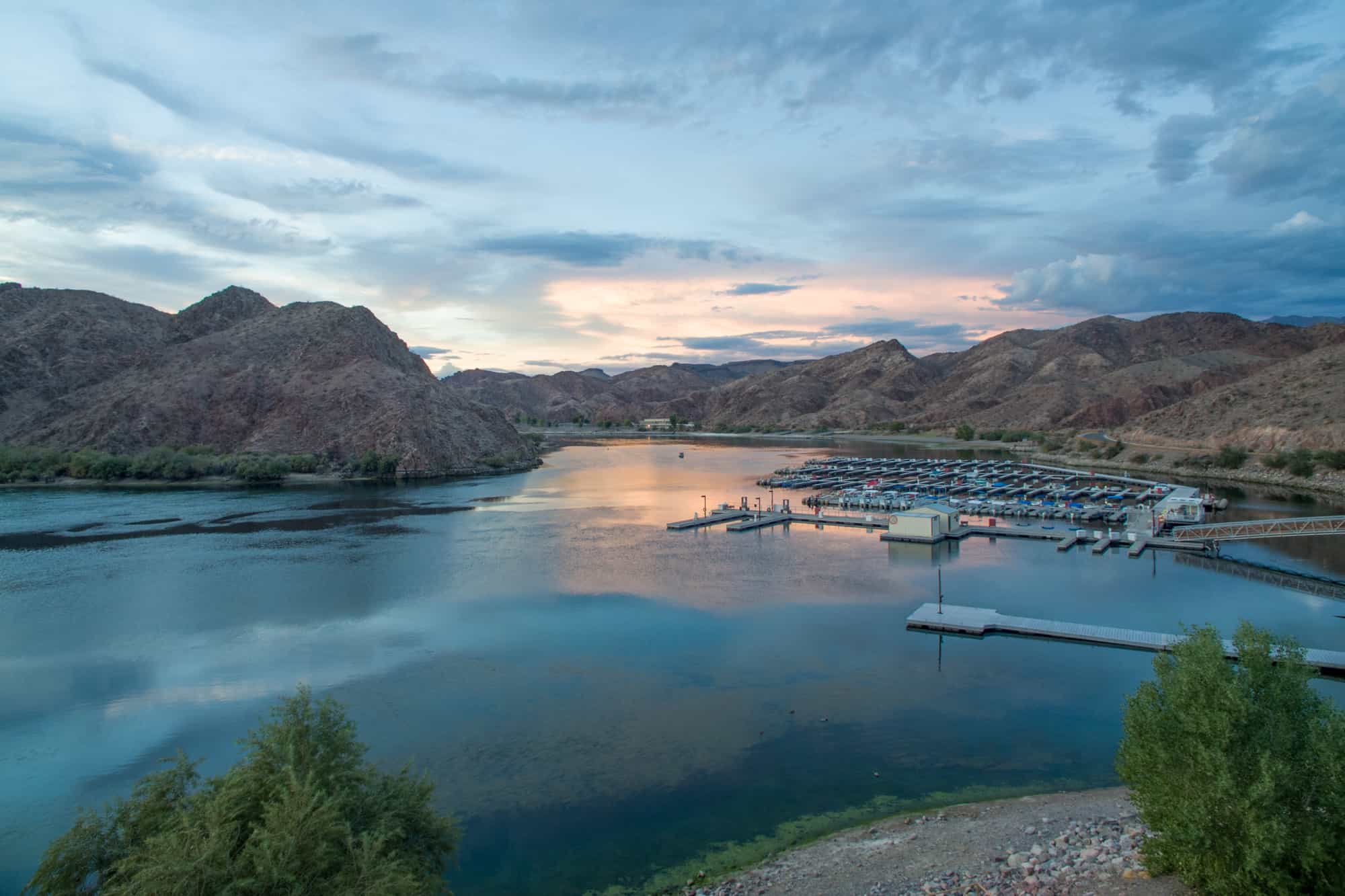 a lake scene with boats anchored along dock sleeves, surrounded by rocky mountains, willow beach is one of the closest beach to tucson options